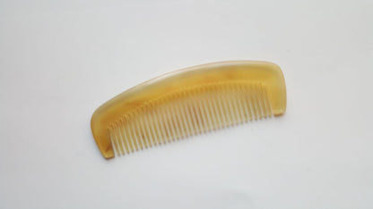  A small sheep horn comb with a curved handle and fine teeth.