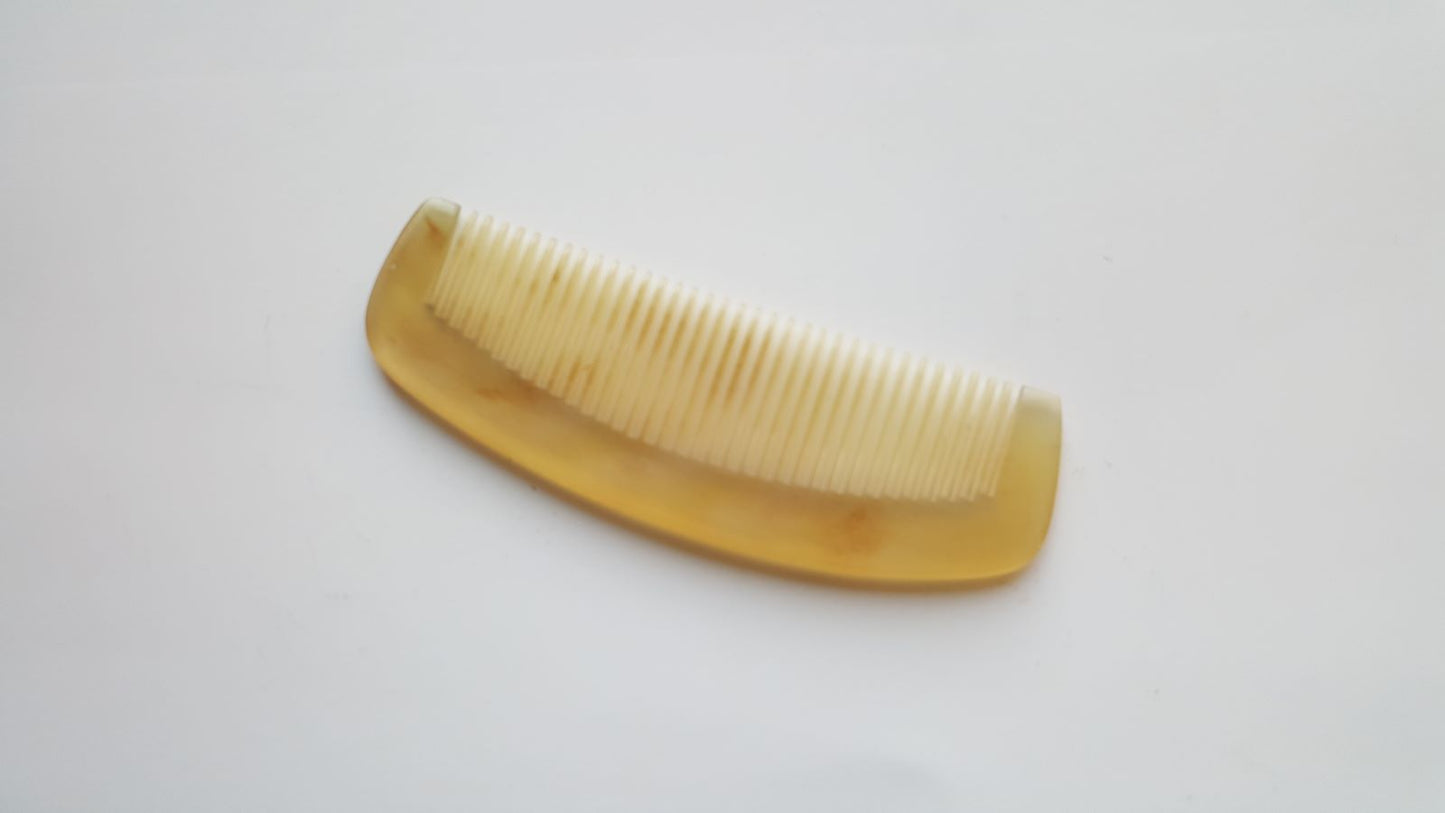 A brown, curved comb with a smooth, polished finish. The comb has fine teeth and is made of natural sheep horn.
