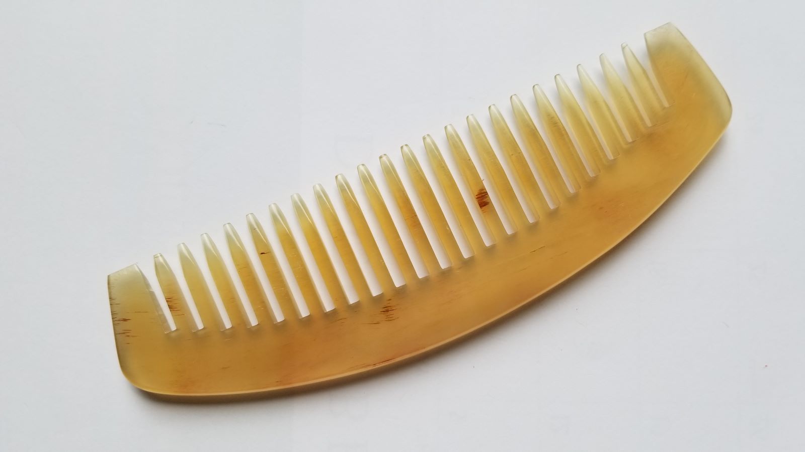Classic sheep horn wide tooth comb in translucent amber, flat lay front view — natural pale yellow to golden honey tone variation — Arakicrafts