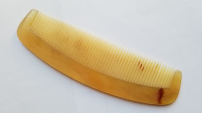 A translucent yellow, curved comb with fine teeth. The comb is made of a natural sheep horn and is designed for hair/beard grooming.
