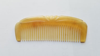 A translucent amber-colored horn hair comb with fine teeth and a decorative carved handle.