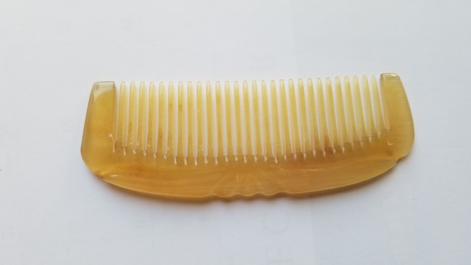 Smooth curved spine of Art Deco sheep horn comb, flat lay side angle showing translucency and natural horn depth — Arakicrafts