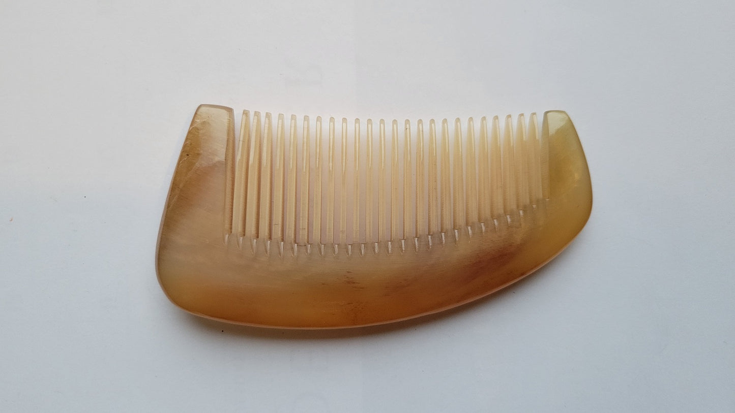 Sheep horn massage comb overhead flat lay, pale amber translucency, smooth arched spine and fine teeth, single-piece horn construction
