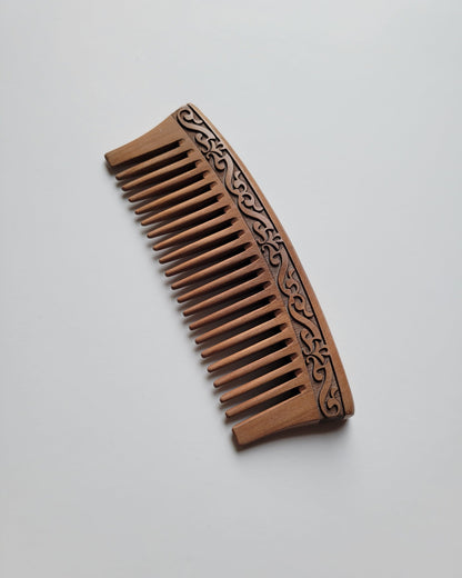 A brown wooden comb with a carved l design. The comb has a curved handle and evenly spaced wide teeth, good for daily hair grooming