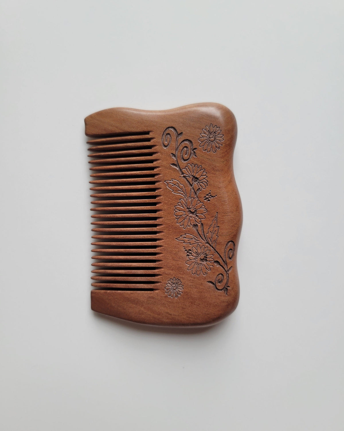 Mini peach wood pocket comb in warm reddish brown with carved flowers, leaves, and curling vines, shown with teeth facing left.