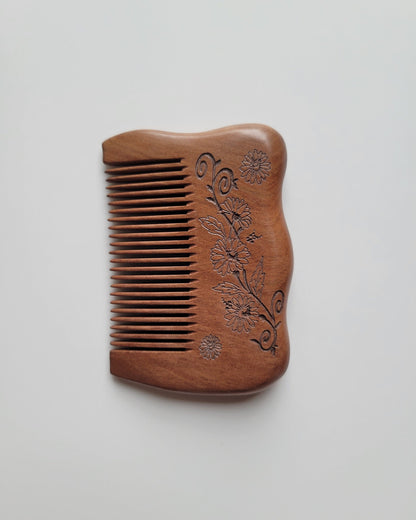 Mini peach wood pocket comb in warm reddish brown with carved flowers, leaves, and curling vines, shown with teeth facing left.