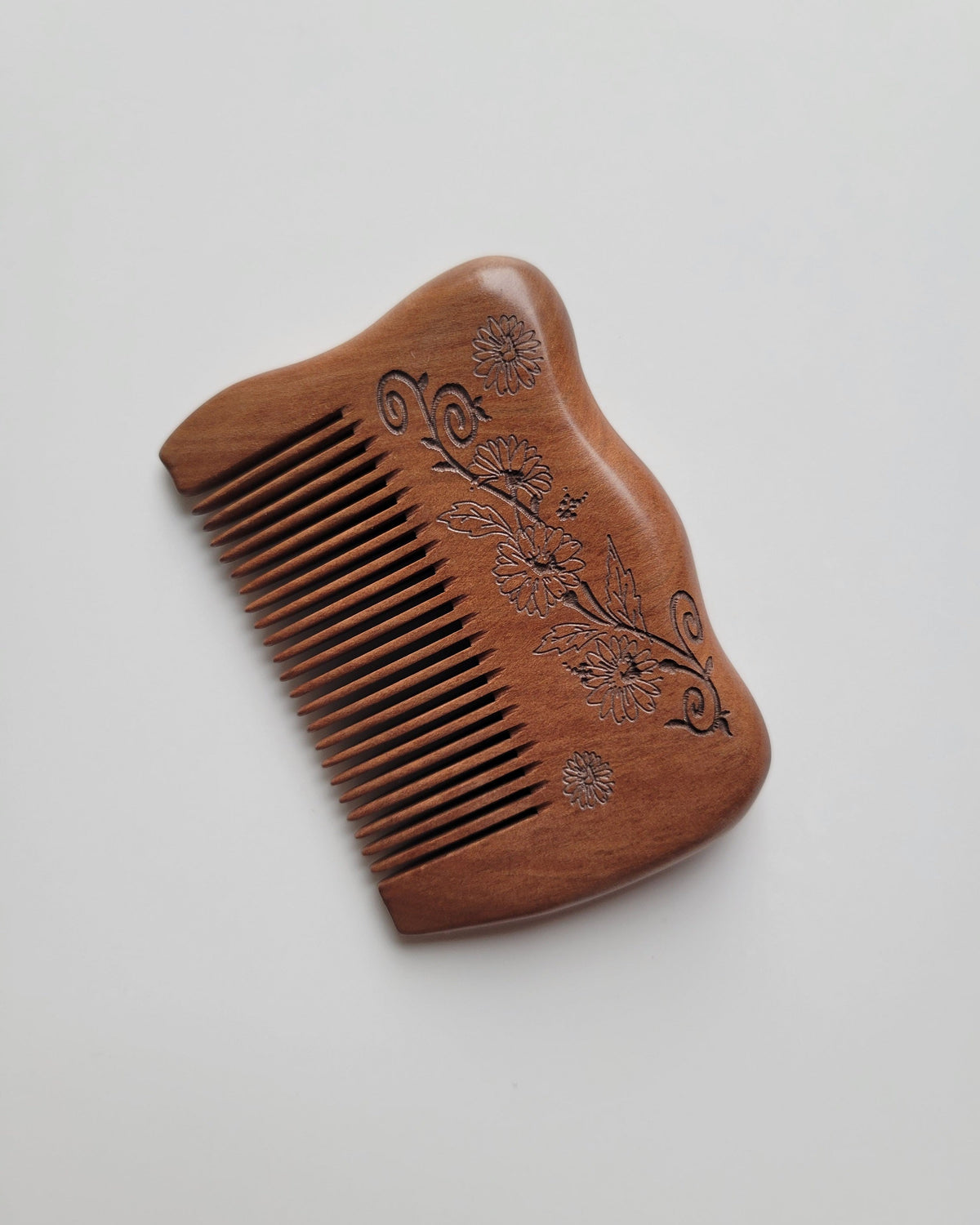 Peach wood comb laid diagonally on a white background, highlighting its fine grain and warm brown color.