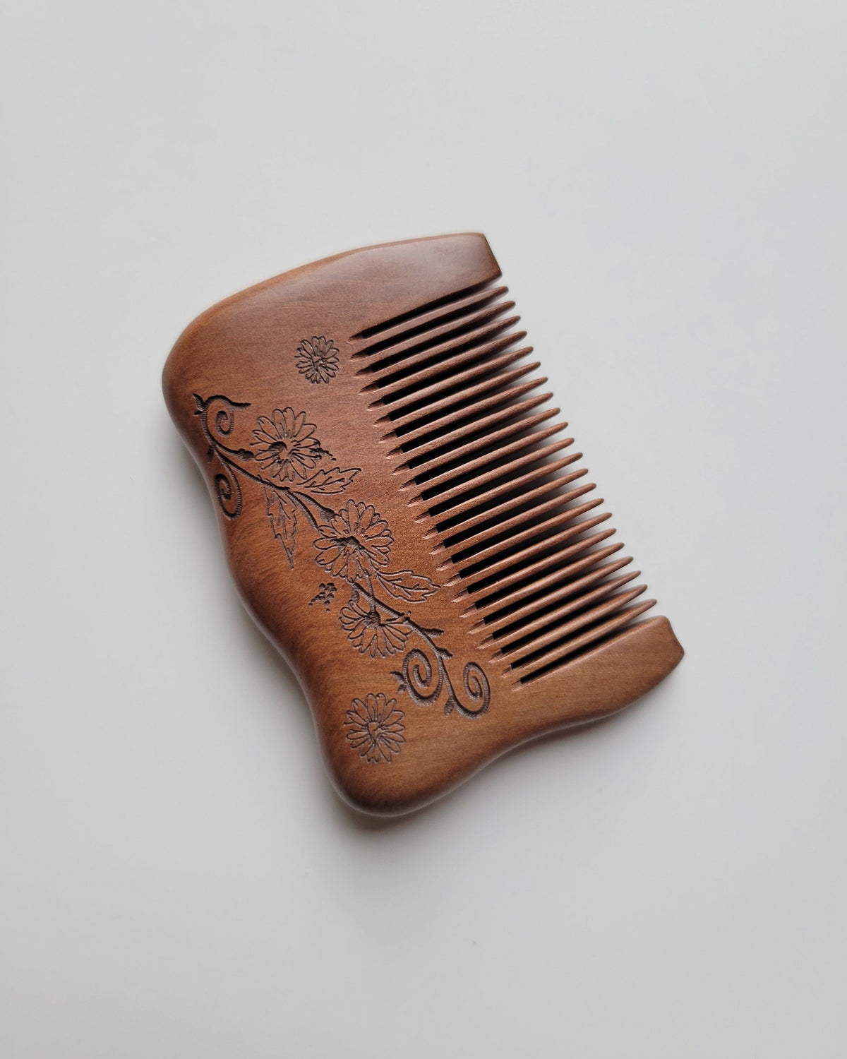 Fine-tooth peach wood comb with 0.15 cm tooth spacing for fine hair grooming, shown diagonally with carved flowers along the grip. good for short and fine hair