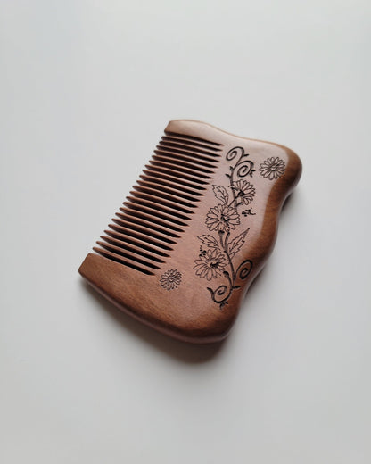Low angled view of the Mini Floral Peach Wood Comb showing its thickness, polished edges, and decorative flower-and-leaf motif.  unique stocking stuffer for her. 