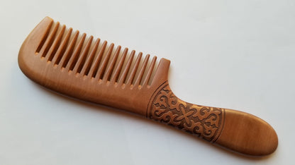 Long handle peach wood wide tooth comb, flat lay side angle showing depth of spiral carving and wood grain — Arakicrafts