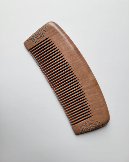 Classic peach wood comb in warm reddish brown with symmetrical carved semicircle motifs at both ends