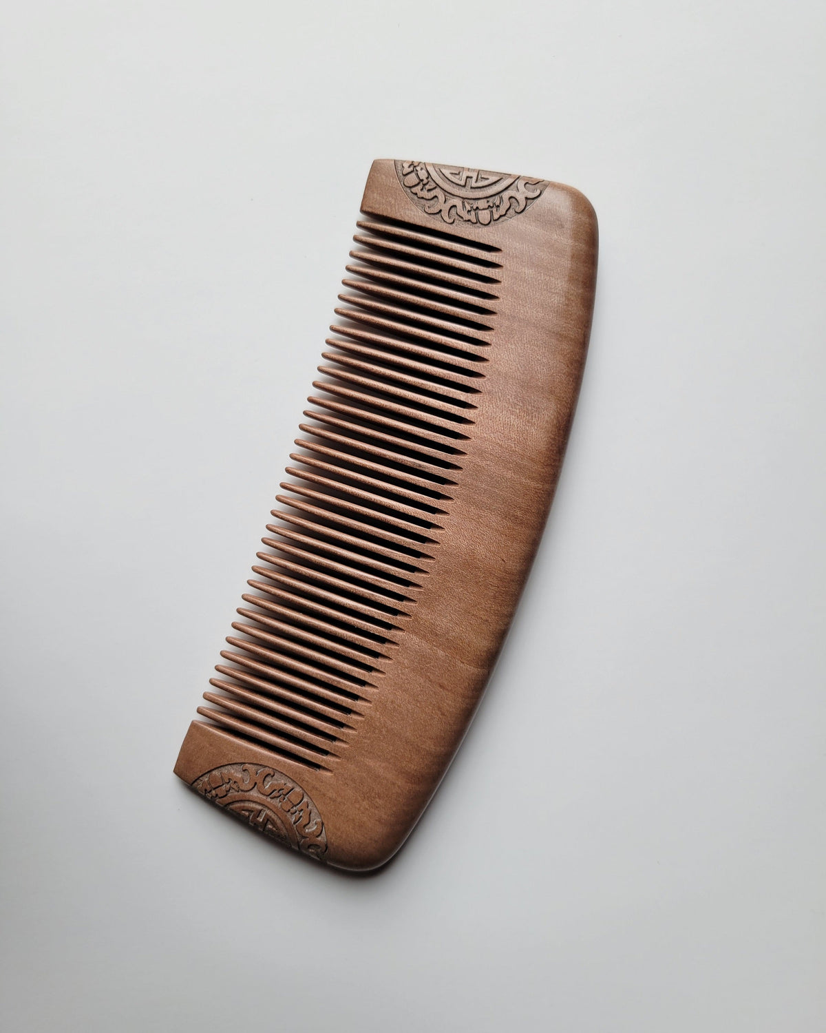 A wooden hair comb with a warm brown finish, featuring carved decorative patterns on the handle and a fine, closely spaced comb teeth