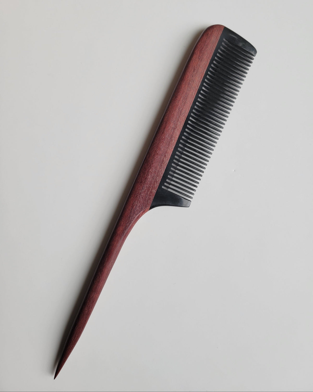 Purple heart wood rat tail comb flat lay, rich reddish-brown hardwood handle, hand-inlaid buffalo horn fine teeth, hair sectioning comb