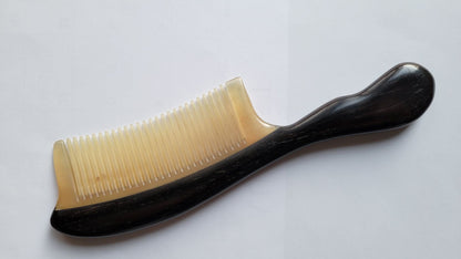 A black and white natural comb with a curved handle. The comb is made of ram horn and African Ebony