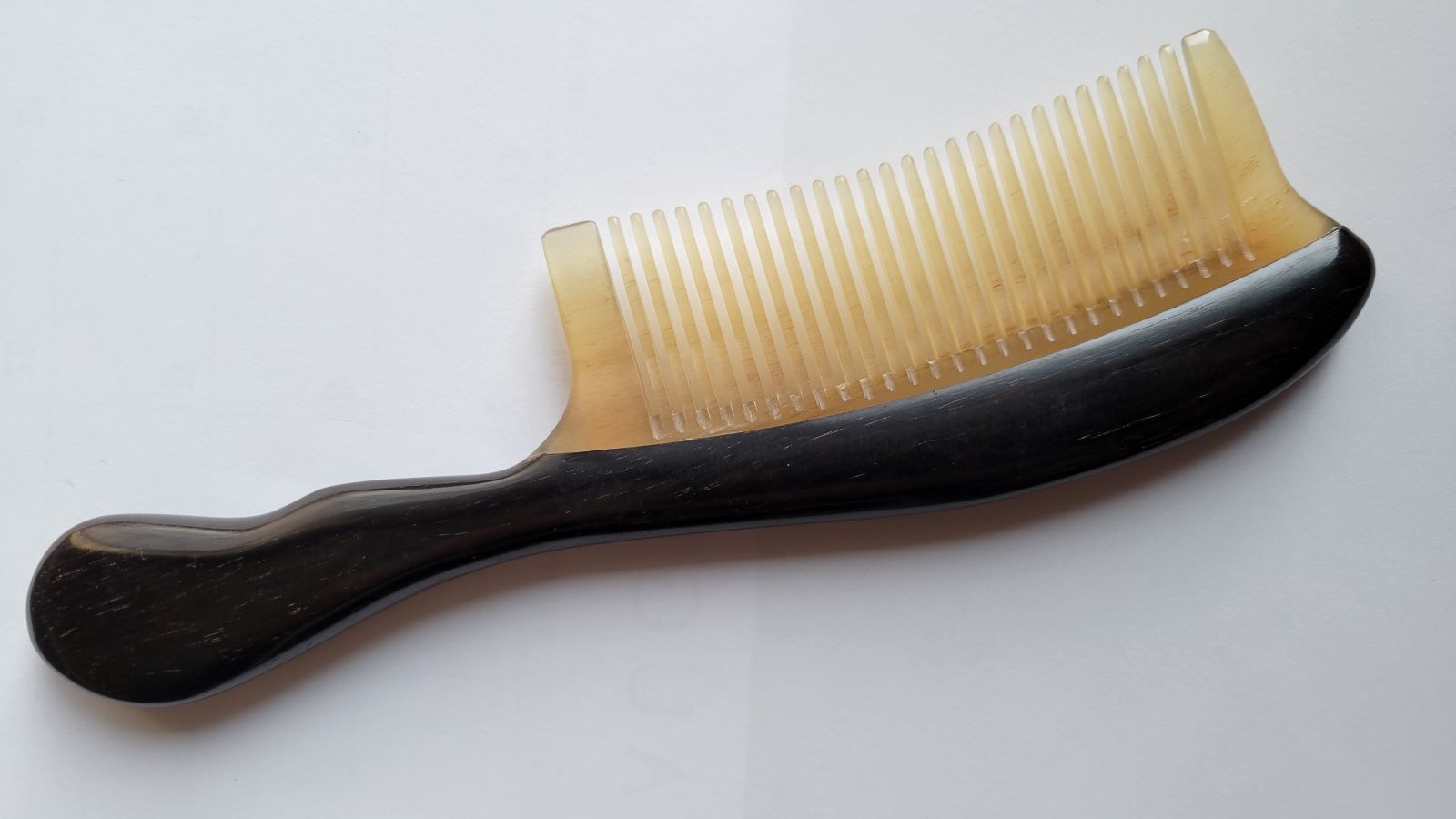 A hand inlayed black wood and ram horn comb with a curved handle. The comb has a teeth tooth design.