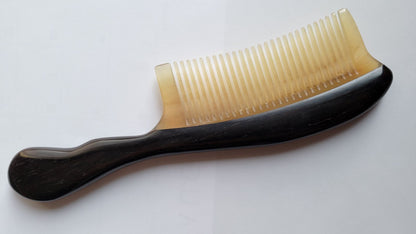 A hand inlayed black wood and ram horn comb with a curved handle. The comb has a teeth tooth design.