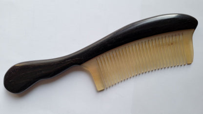 A black and cream color comb with a curved wooden handle. The comb has fine teeth and is made of African ebony and ram horn.