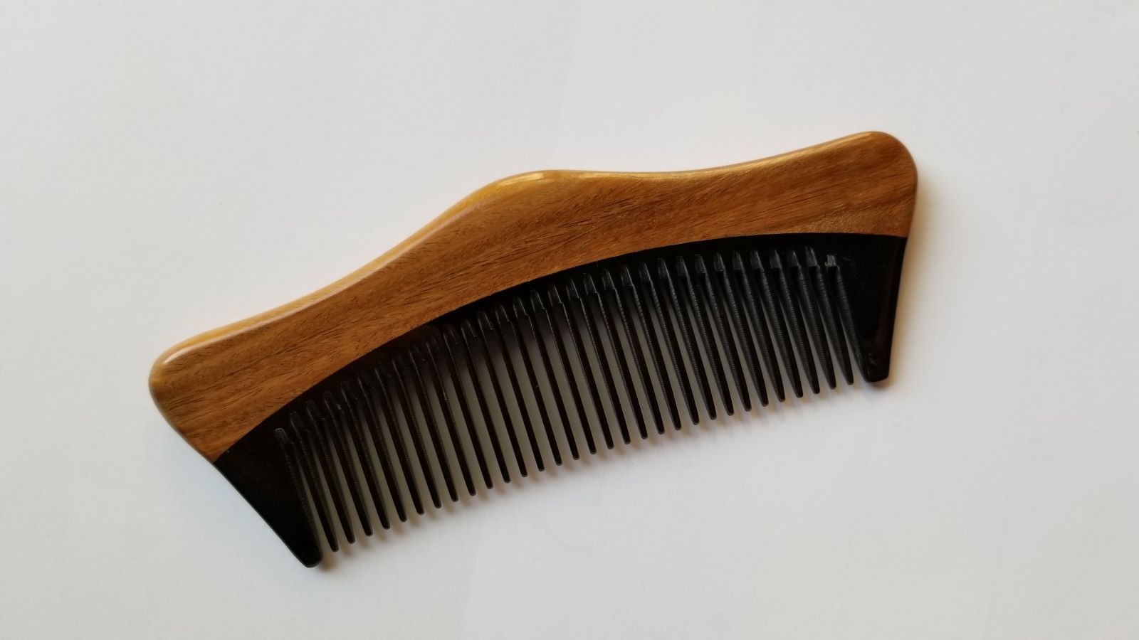 Anti-static buffalo horn beard comb for men, flat lay overhead view — Arakicrafts.  The comb has a curved, ergonomic shape, and is designed for grooming hair.