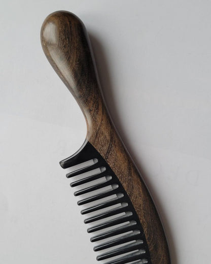 A wooden comb with a dark brown handle and black horn teeth. The handle has a rounded end for easy grip. The comb's teeth are evenly spaced, and the wood grain is visible.