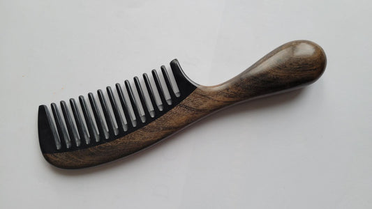 A wooden comb with a dark brown handle and black horn teeth. The handle has a rounded end for easy grip. The comb's teeth are evenly spaced, and the wood grain is visible.