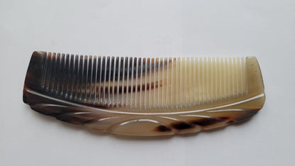 A brown and white tortoiseshell comb with a curved handle and a decorative design. The comb has a smooth, polished finish.