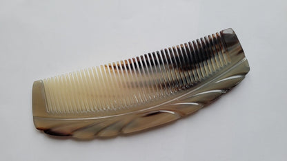 A curved, brown and white comb made of yak horn with a decorative design on the upper handle section.