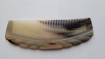 A brown and beige tortoiseshell comb with a decorative design on the top. The comb has fine teeth and is curved. It was designed for hair grooming.