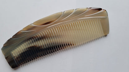 A brown and beige tortoiseshell comb with a curved design. The comb has fine teeth and a smooth, polished finish. Each piece is unique and make it a one of kind gift. 