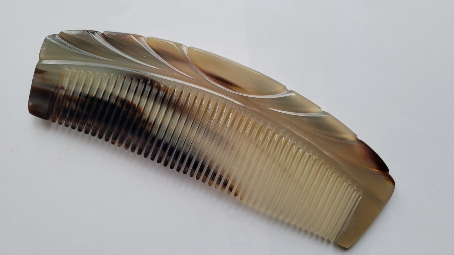 A brown and white tortoiseshell comb with a curved shape and a decorative design on the top. It is made of horn The comb has fine teeth - Front View