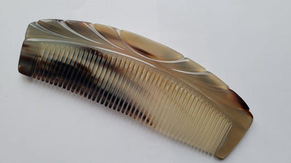 A brown and white tortoiseshell comb with a curved shape and a decorative design on the top. It is made of horn The comb has fine teeth - Front View