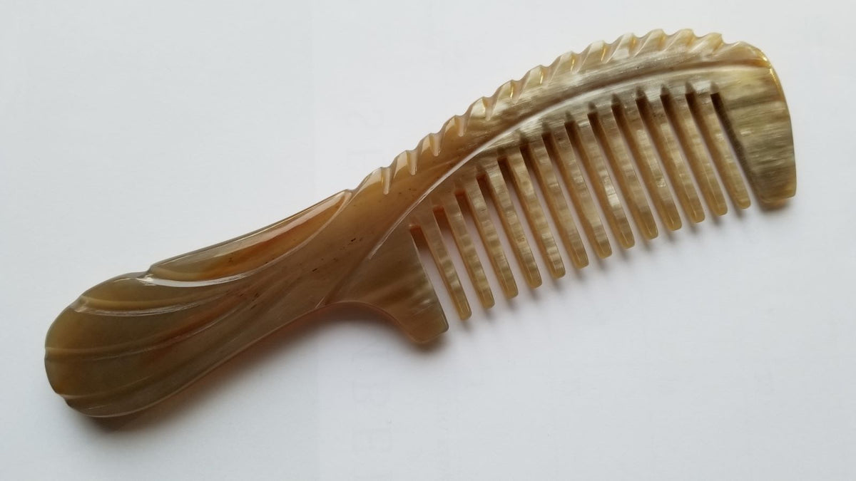 Close-up of carved shallow indentations along the top edge of yak horn comb handle — Arakicrafts. It has white streaks on one side of the comb 